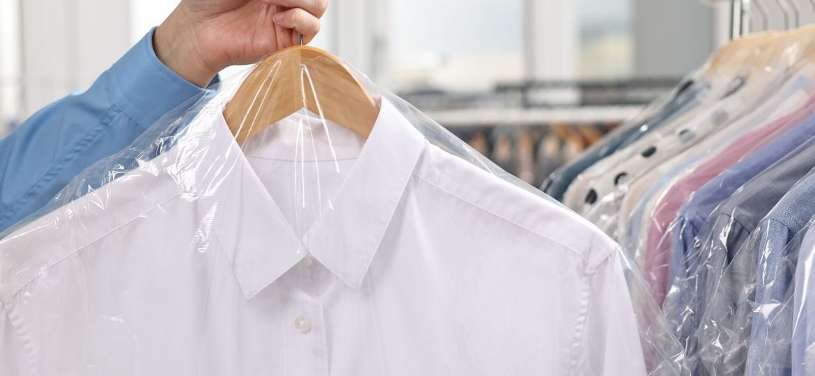 Dry-cleaning service. Woman holding shirt in plastic bag indoors